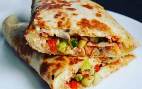 Złocista tortilla z jajkiem, serem i szynką, wypełniona warzywami, usmażona na patelni. Pyszne danie na szybki posiłek.