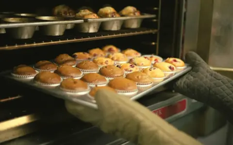 Rękawice wyjmują z piekarnika blachę z gotowymi muffinkami, które idealnie nadają się do przepisu na wilgotne i puszyste muffinki.