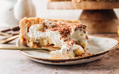 Pyszne ciasto migdałowiec z bananami i bitą śmietaną, posypane czekoladą. Idealne na deser!