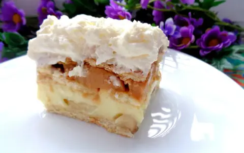 Szybkie ciasto z bananami i budyniem, warstwowe, z kremem i bitą śmietaną, na talerzu, w tle fioletowe kwiaty.