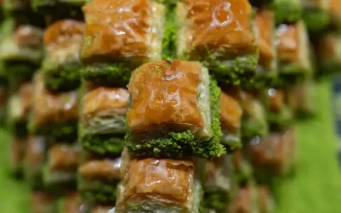 Słodka baklava, co to za przysmak? Warstwy ciasta filo, orzechów i syropu, posypane zielonymi pistacjami.