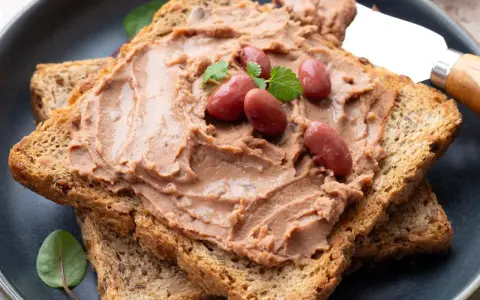 Pyszna pasta z czerwonej fasoli na chrupiących tostach pełnoziarnistych, udekorowana fasolkami i listkami ziół.