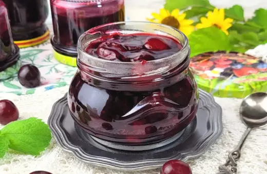 Słoiczek pełen wiśniowej frużeliny, obok świeże wiśnie i listki mięty.