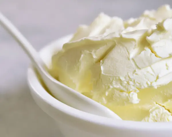 Kremowa masa w białej miseczce z łyżką. Idealna do deserów, gdy szukasz, czym zastąpić mascarpone.