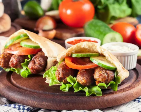 Dwa pyszne **ćevapi** w bułce z sałatą, pomidorem i ogórkiem, podane z sosem.