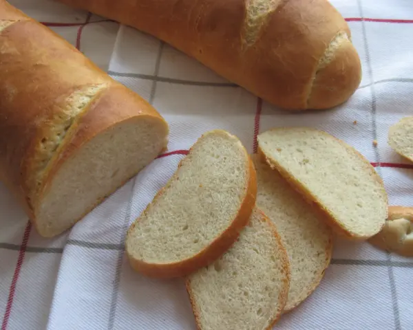Chrupiąca bułka wrocławska, pokrojona w kromki, leży obok całej bagietki na lnianym obrusie.