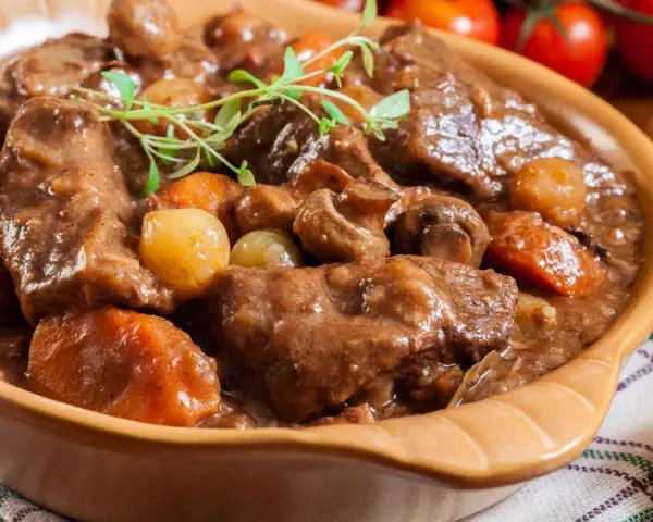 Gęsta, aromatyczna łata wołowa z warzywami i grzybami, podana w glinianej misie, udekorowana gałązką ziół.