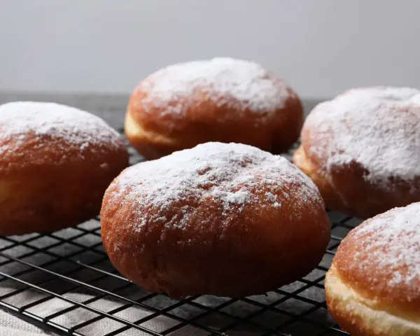 Szybkie pączki z piekarnika, oprószone cukrem pudrem, wyglądają apetycznie na czarnej kratce.
