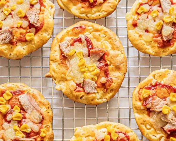 Mini pizze z serka wiejskiego, z kukurydzą i kawałkami mięsa, ułożone na metalowej kratce.