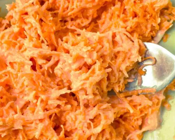 Pyszna surówka z marchewki jak z restauracji, kremowa i apetyczna. Widoczna łyżka widelca zagłębiająca się w jej wnętrze.