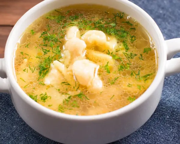 Aromaticzna zupa zacierkowa z koperkiem, podana w białej miseczce na granatowym obrusie.