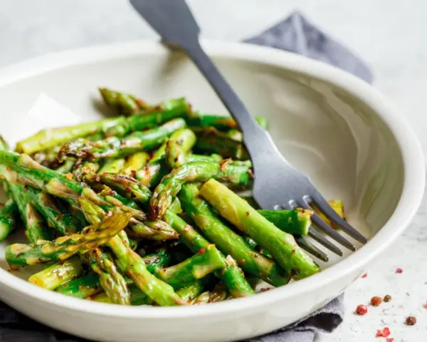 Miseczka pełna pysznych, lekko przypieczonych zielonych szparagów, gotowych do zjedzenia. Widelec czeka, by zacząć ucztę.