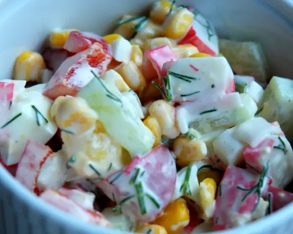 Pyszna, kremowa sałatka z surimi, kukurydzą, ogórkiem i jajkiem, posypana świeżym koperkiem. Idealna na każdą okazję, to najlepsza sałatka z surimi!