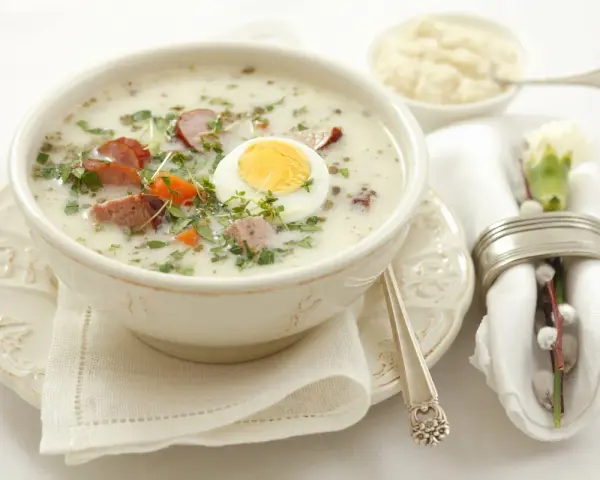 Aromaticzny żurek z białą kiełbasą i jajkiem, podany w misce, z dodatkiem ziół i marchewki. Idealny prosty przepis na żurek.