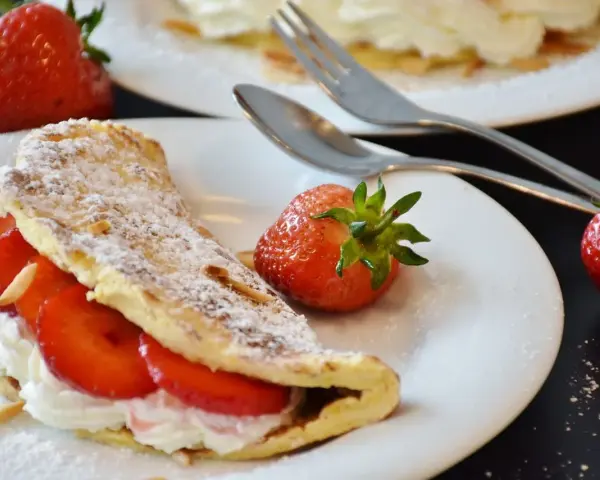 Słodki omlet z truskawkami i bitą śmietaną, posypany cukrem pudrem. Idealny przepis na omlet na słodko.