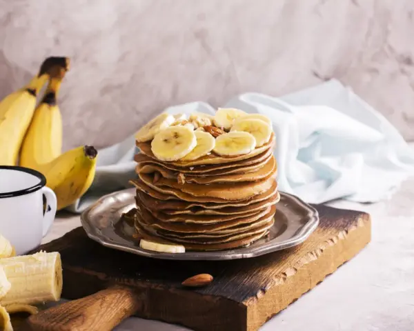 Stos naleśników z plasterkami banana i orzechami. Idealny pomysł, co zrobić z bananów na pyszne śniadanie.