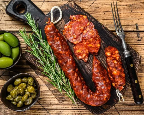 Chorizo co to? Pikantna, wędzona kiełbasa na desce z oliwkami, kaparami i rozmarynem. Idealna przekąska.