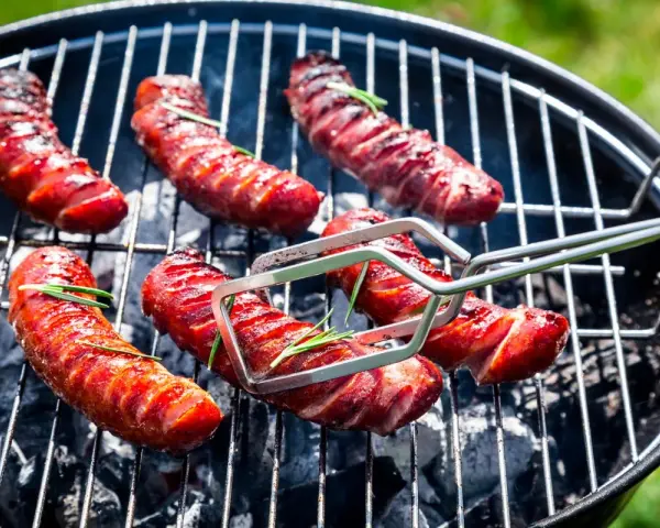 Soczysta kiełbasa na grilla, rumieniąca się nad żarem. Aromatyczny rozmaryn dodaje jej wyjątkowego smaku.