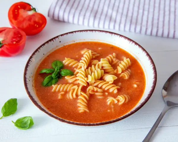 Aksamitna zupa pomidorowa z makaronem fusilli, ozdobiona bazylią. Idealne jakie przyprawy do zupy pomidorowej? Świeże pomidory obok sugerują prostotę i smak.