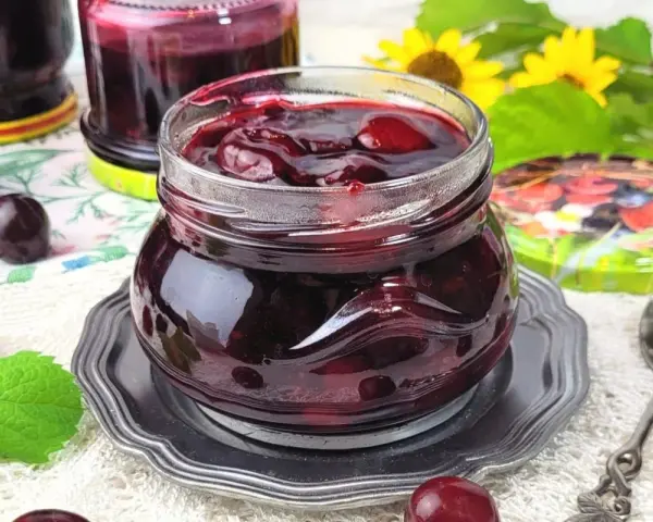 Słoiczek pełen wiśniowej frużeliny, obok świeże wiśnie i listki mięty.