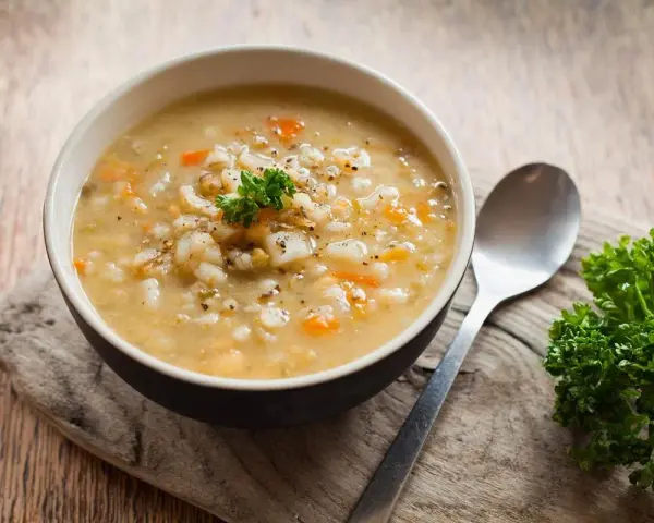 A miseczka parującego krupniku, pachnącego jak zupa krupnik przepis babci. Obok łyżka i gałązka natki pietruszki.