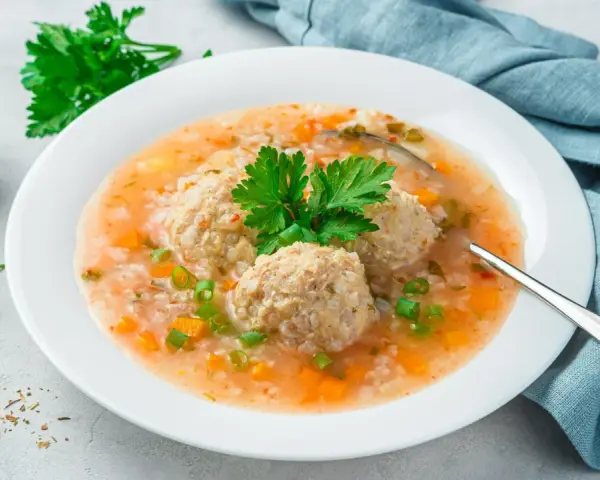 Szybka zupa na obiad z klopsikami, ryżem i warzywami, udekorowana natką pietruszki.
