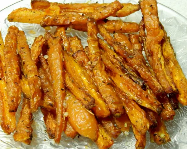Chrupiące, pieczone frytki z marchewki, przyprawione ziołami i czosnkiem, kuszą apetycznym wyglądem na talerzu.