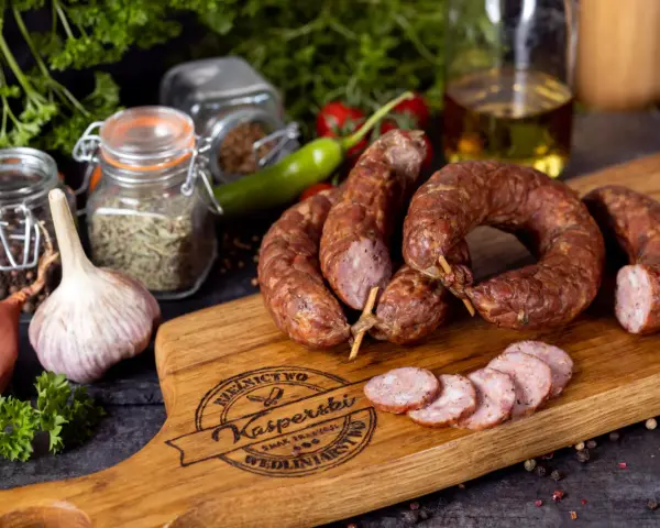 Na drewnianej desce leży pyszna, wędzona kiełbasa jałowcowa, obok czosnek, cebula i przyprawy.