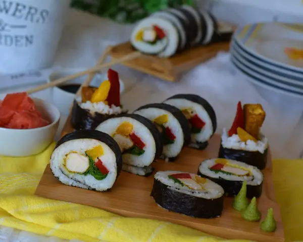 Pyszne sushi z kurczakiem, papryką i mango. Podane na desce z dodatkami: marynowanym imbirem i wasabi.