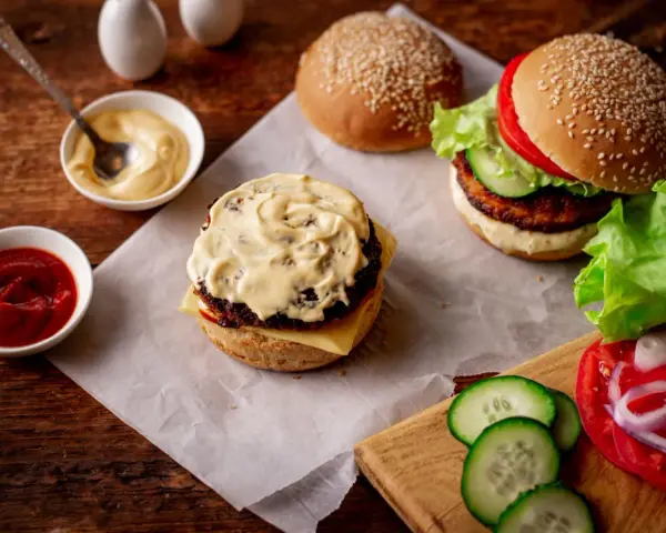 Pyszny sos do burgera, ketchup i majonez czekają na idealne kanapki. Obok świeże warzywa i bułki z sezamem.