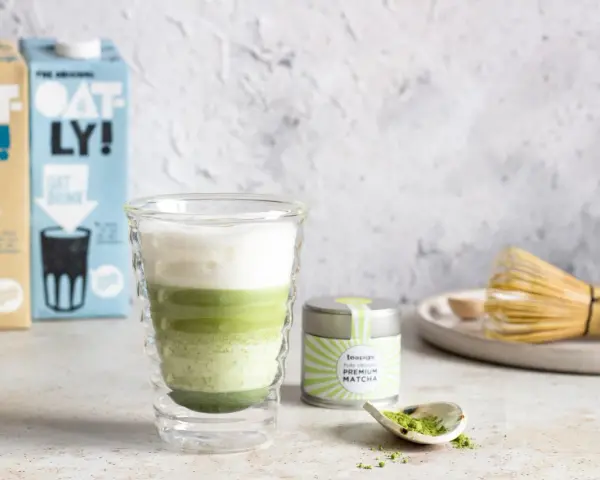 Zielony napój warstwowy w szklance, obok puszka z napisem "PREMIUM MATCHA" i bambusowa miotełka. To jest właśnie co to matcha.
