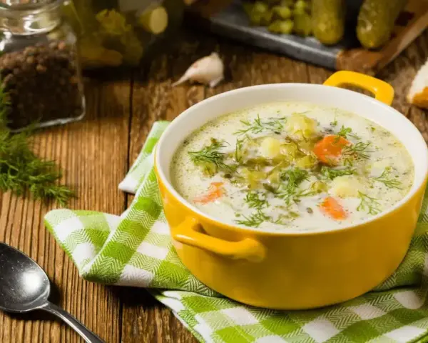Zupa ogórkowa z koperkiem, ziemniakami i marchewką. W tle słoik z pieprzem, czosnek i ogórki kiszone. Idealne jakie przyprawy do zupy ogórkowej?