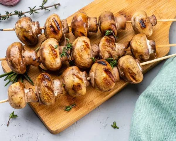 Grillowane pieczarki na drewnianej desce, przyprawione ziołami. Idealne na letnie przyjęcie.