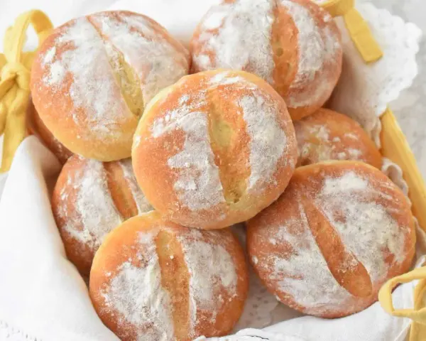Koszyk pełen świeżych, puszystych bułek ziemniaczanych, posypanych mąką. Idealne na śniadanie.