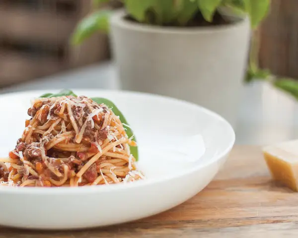 Pyszne spaghetti bolognese, przygotowane według oryginalnego przepisu, posypane parmezanem i udekorowane listkiem bazylii.