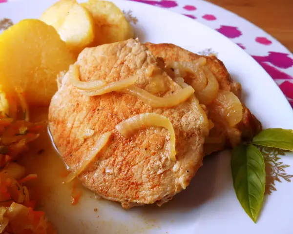 Pyszny schab w cebuli, idealny na niedzielny obiad, podany z ziemniakami i surówką.
