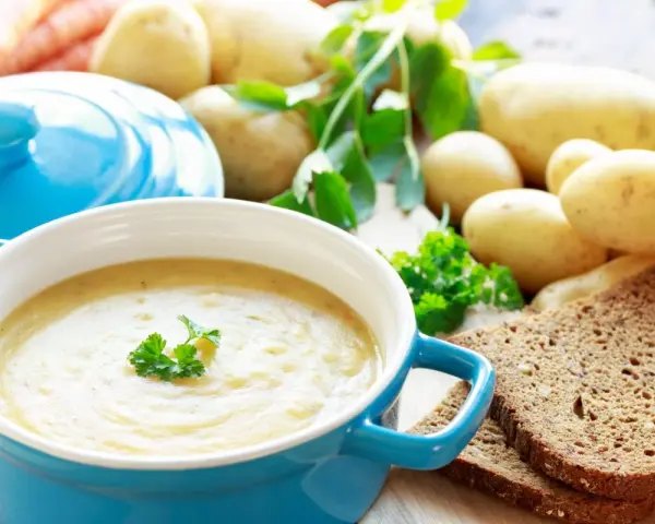 Aksamitna zupa ziemniaczana, przepis babci, z chlebem i świeżymi ziemniakami w tle.