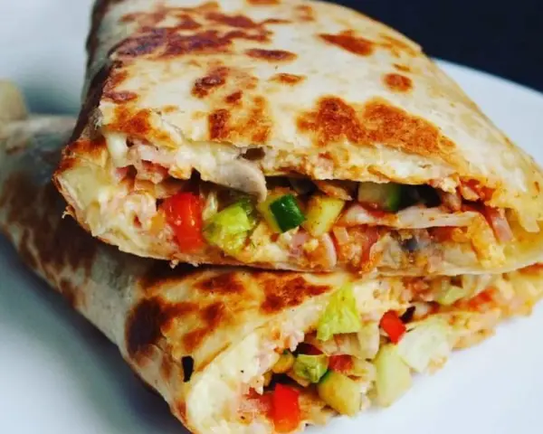 Złocista tortilla z jajkiem, serem i szynką, wypełniona warzywami, usmażona na patelni. Pyszne danie na szybki posiłek.
