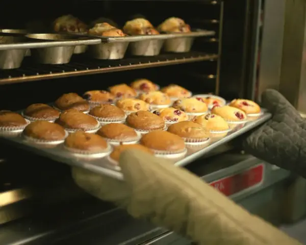 Rękawice wyjmują z piekarnika blachę z gotowymi muffinkami, które idealnie nadają się do przepisu na wilgotne i puszyste muffinki.