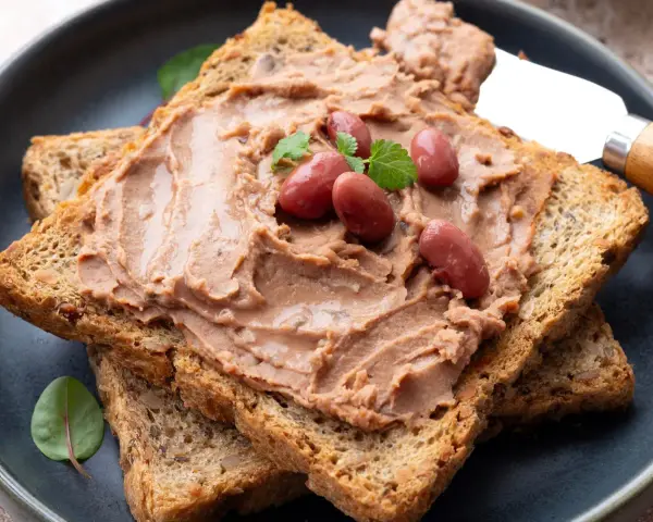 Pyszna pasta z czerwonej fasoli na chrupiących tostach pełnoziarnistych, udekorowana fasolkami i listkami ziół.