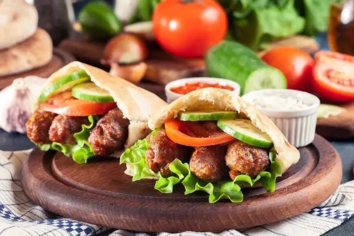 Dwa pyszne **ćevapi** w bułce z sałatą, pomidorem i ogórkiem, podane z sosem.