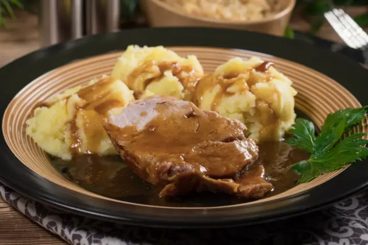 Karkówka w sosie własnym z purée ziemniaczanym, udekorowana natką pietruszki. Pyszny sos do karkówki idealnie komponuje się z ziemniakami.