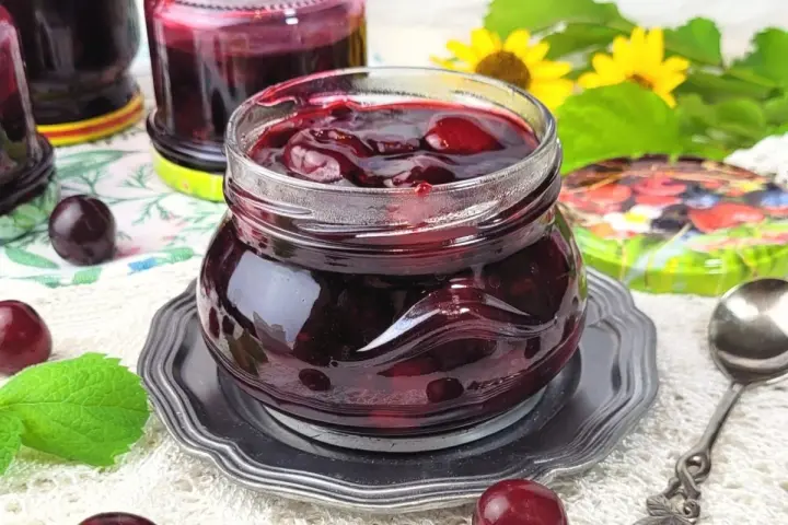 Słoiczek pełen wiśniowej frużeliny, obok świeże wiśnie i listki mięty.