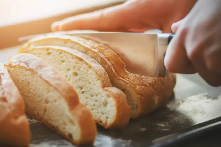 Dłoń kroi świeży chleb na kromki. Zastanawiasz się, jak odświeżyć chleb? Ten obrazek pokazuje, jak zacząć.