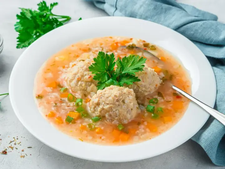 Szybka zupa na obiad z klopsikami, ryżem i warzywami, udekorowana natką pietruszki.