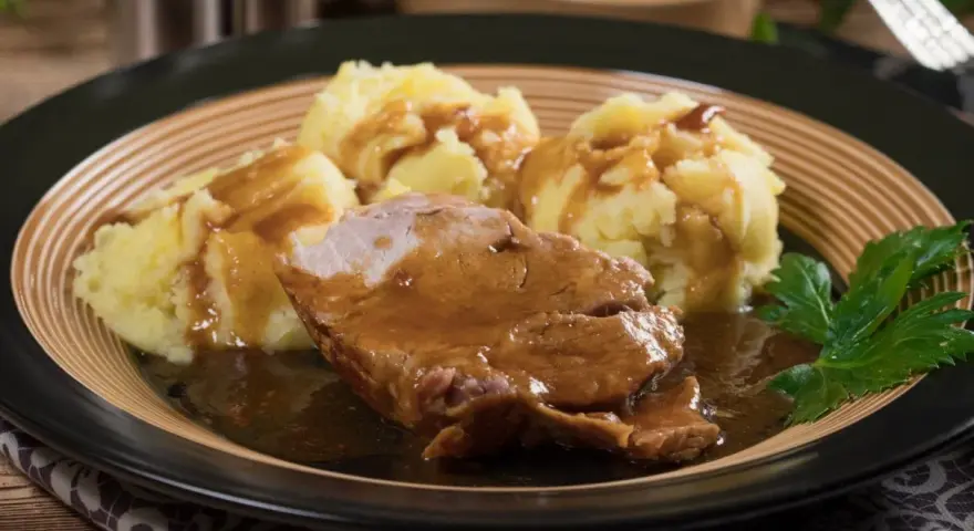 Karkówka w sosie własnym z purée ziemniaczanym, udekorowana natką pietruszki. Pyszny sos do karkówki idealnie komponuje się z ziemniakami.