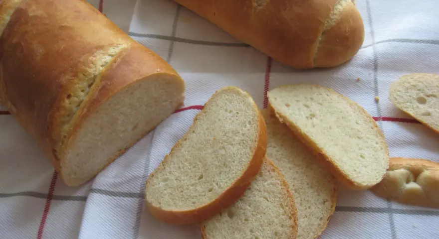 Chrupiąca bułka wrocławska, pokrojona w kromki, leży obok całej bagietki na lnianym obrusie.