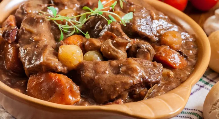 Gęsta, aromatyczna łata wołowa z warzywami i grzybami, podana w glinianej misie, udekorowana gałązką ziół.
