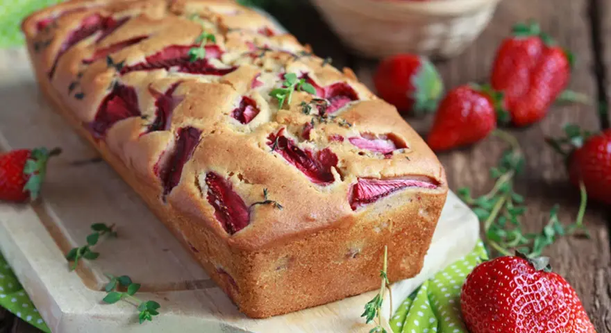 Wilgotne ciasto jogurtowe z owocami, pachnące świeżymi truskawkami i ziołami, kusi apetycznym wyglądem.