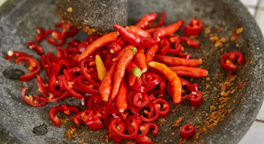 Ostry jak diabli! Całe mnóstwo czerwonych papryczek chili, niektóre pokrojone w plasterki, leżą w kamiennym moździerzu. To zapowiada najostrzejszą paprykę!